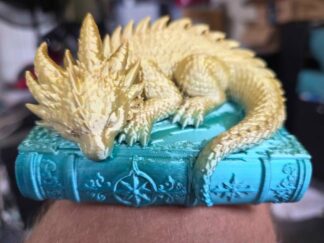 Golden sleeping dragon resting on a detailed teal fantasy book